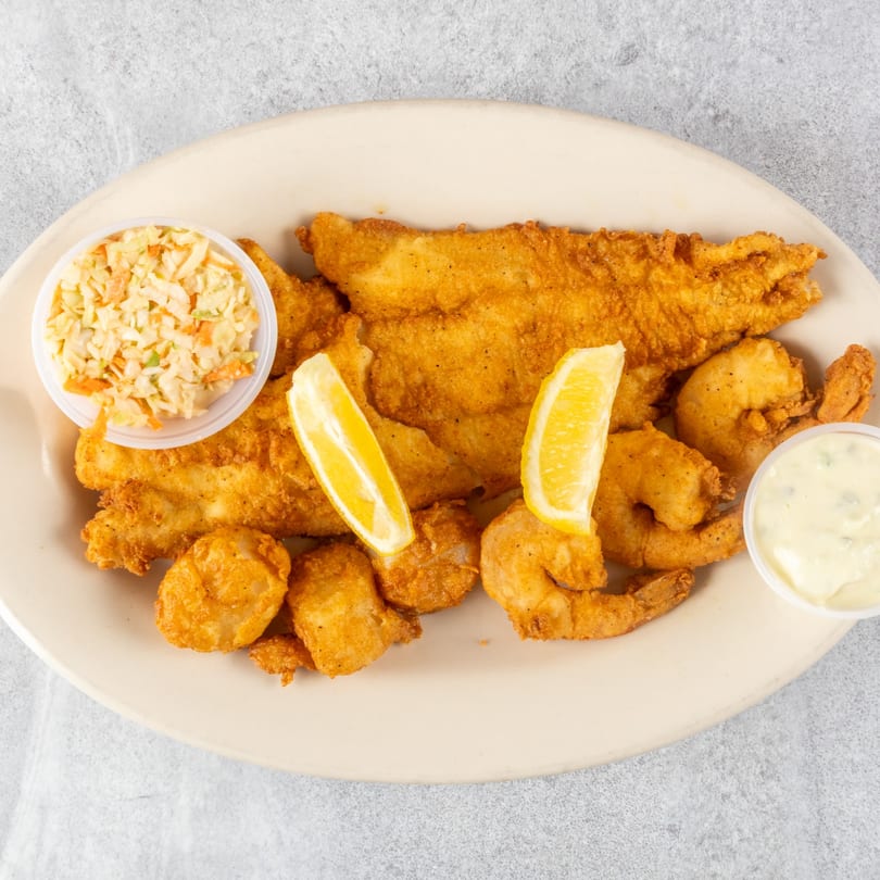 Fried fish, shrimp, and scallops with lemon wedges, coleslaw, and tartar sauce on a plate.