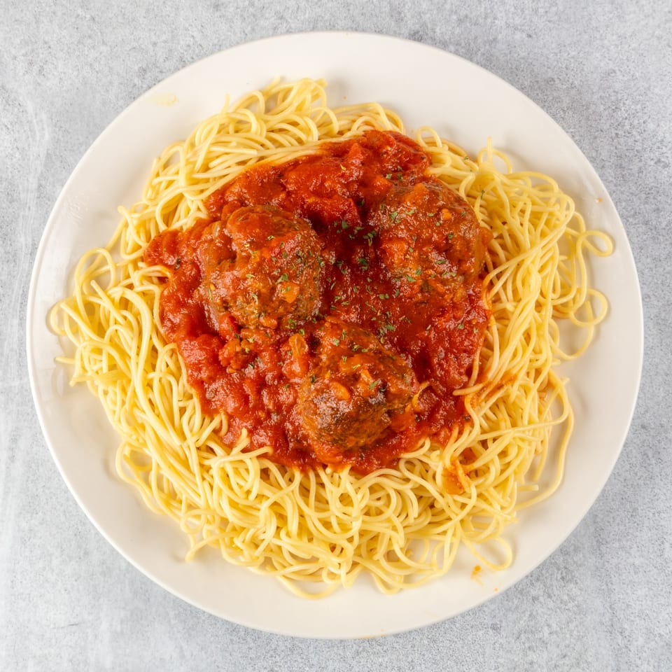 Spaghetti with three large meatballs covered in red marinara sauce, garnished with herbs.