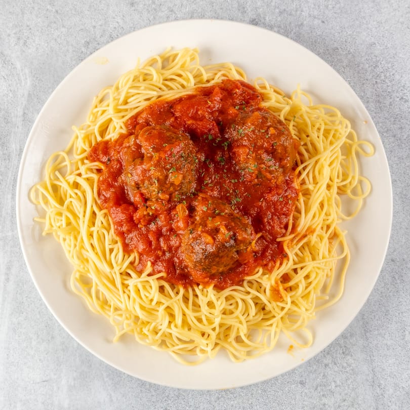 Spaghetti with three large meatballs covered in red marinara sauce, garnished with herbs.
