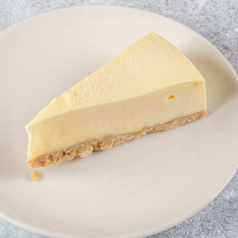 A slice of classic cheesecake with a graham cracker crust on a white plate.
