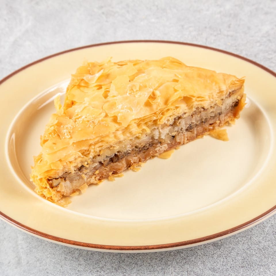 A triangular slice of golden-brown baklava with flaky layers and a nutty filling on a yellow plate.