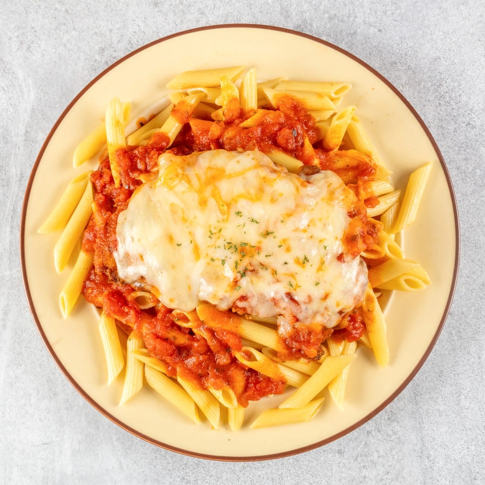 Chicken Parmesan with penne pasta and marinara sauce, topped with melted mozzarella cheese and parsley.
