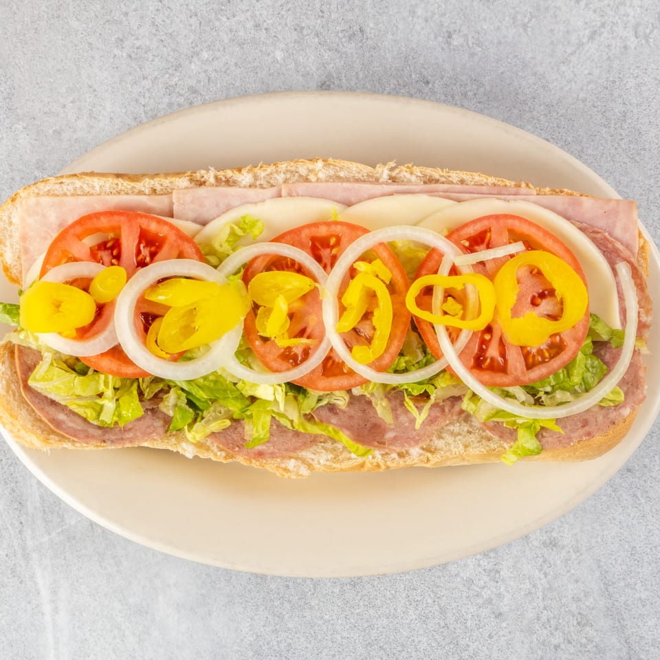 A Zoe's Pizza and Seafood sub sandwich with ham, salami, cheese, lettuce, tomatoes, onions, and peppers.