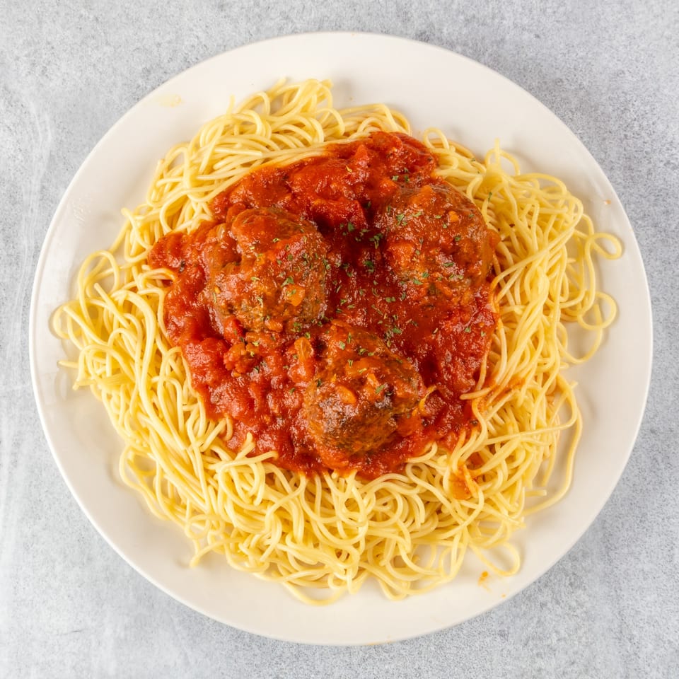 Spaghetti with three meatballs and red marinara sauce, garnished with parsley on a white plate.
